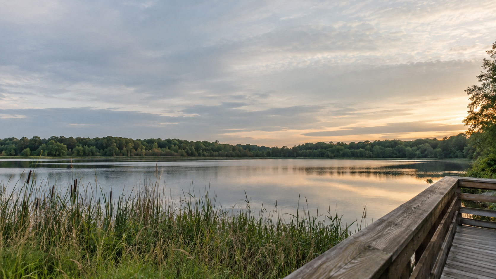 A calm lake at sunset beside a wooden boardwalk